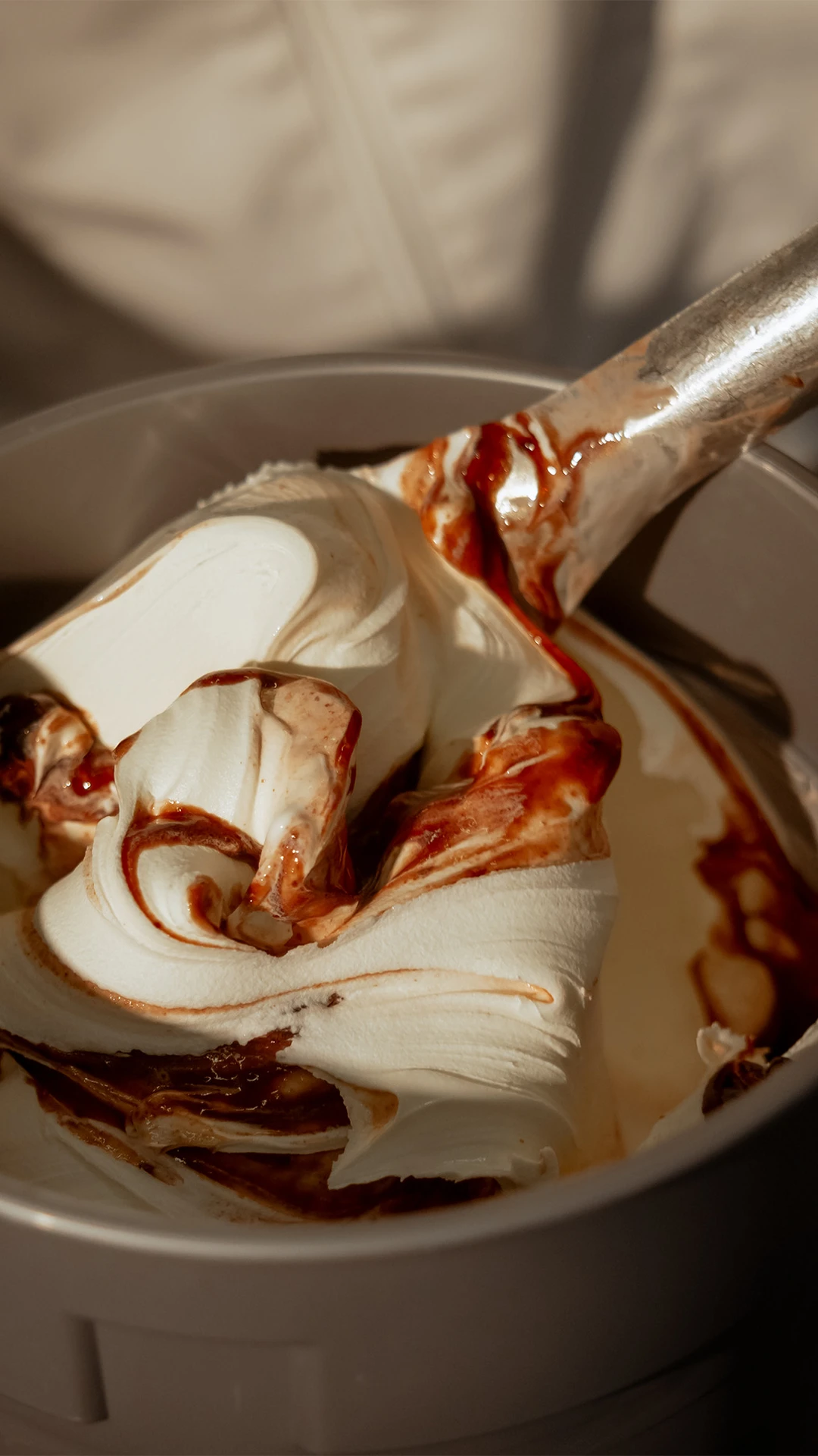 Close-up of a hand stirring fresh, swirled gelato with ripples in a container,