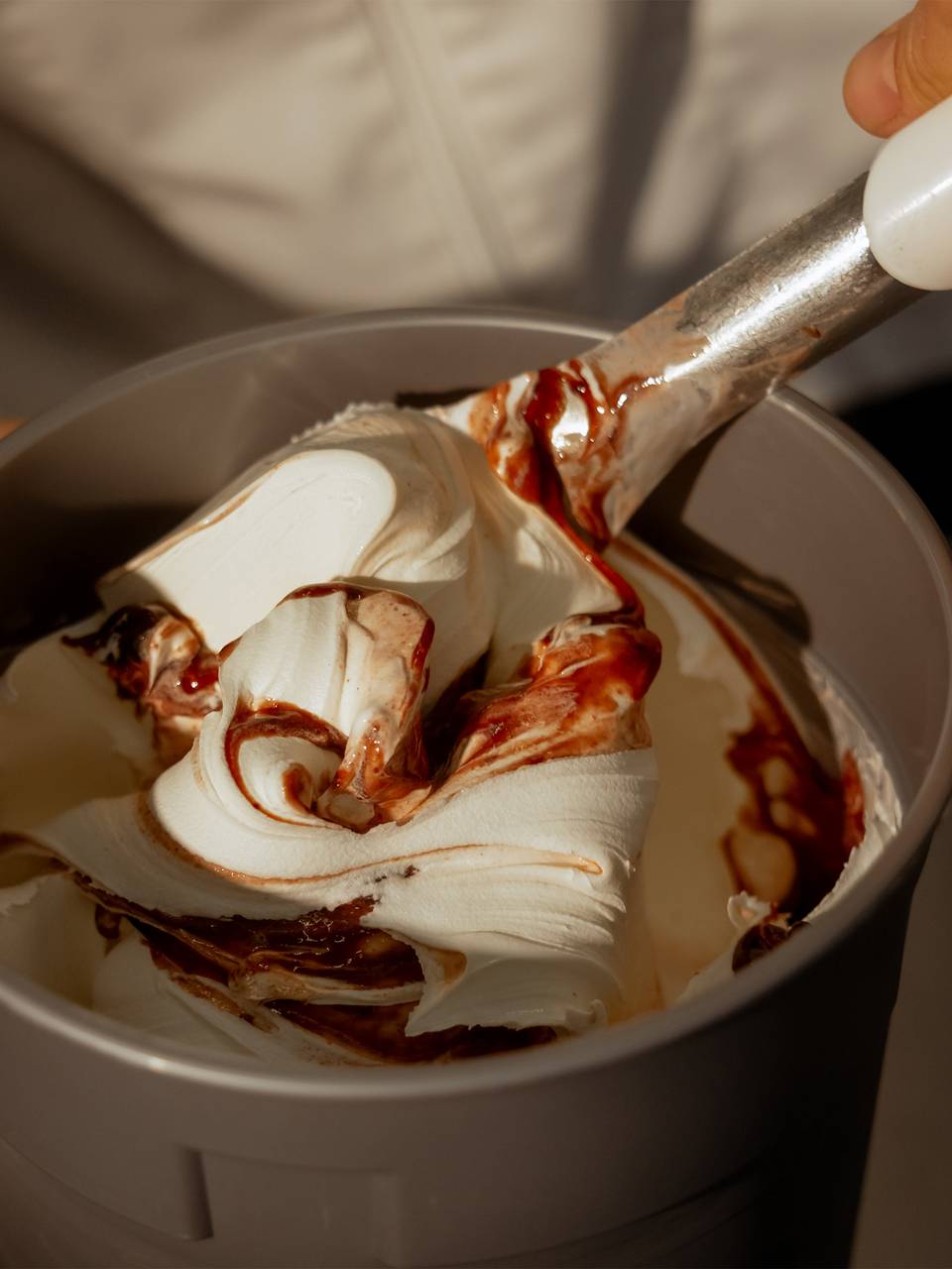 Close-up of a hand stirring fresh, swirled gelato with ripples in a container,