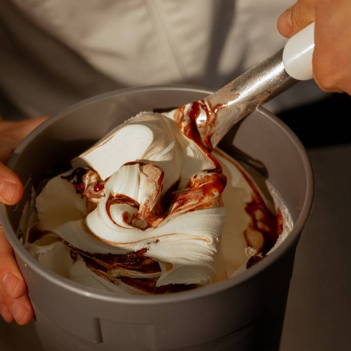 Close-up of a hand stirring fresh, swirled gelato with ripples in a container,