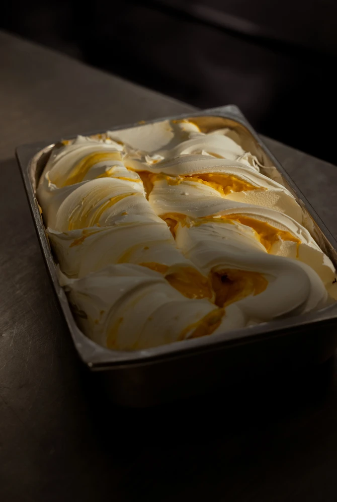 A metal tray filled with creamy, swirled gelato, combining white and rich orange tones.