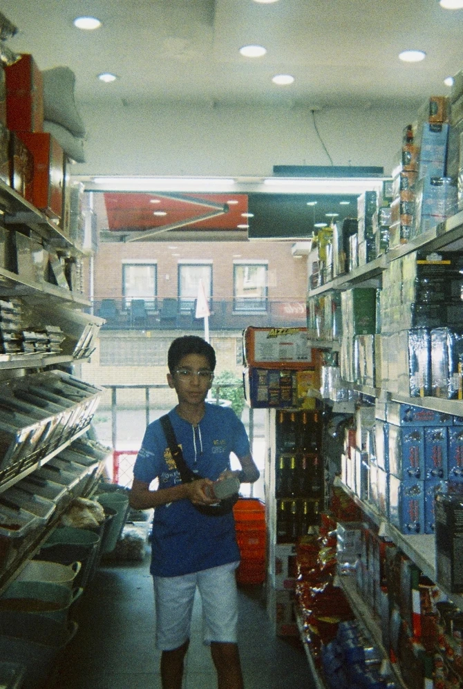 A person in a blue shirt and white shorts stands in a narrow grocery aisle, holding items.