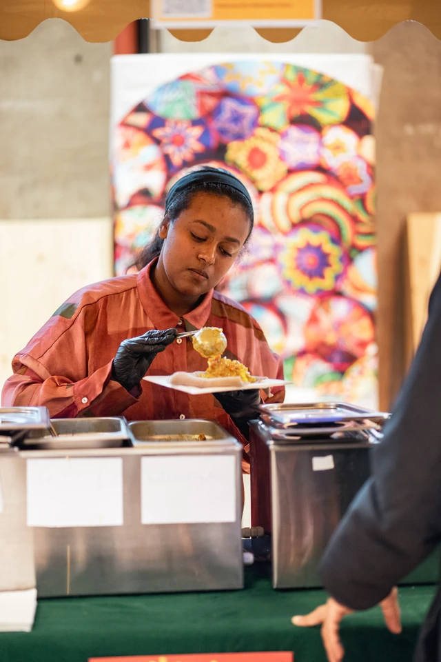 A woman serving food from a colourful African Food Festival stall.