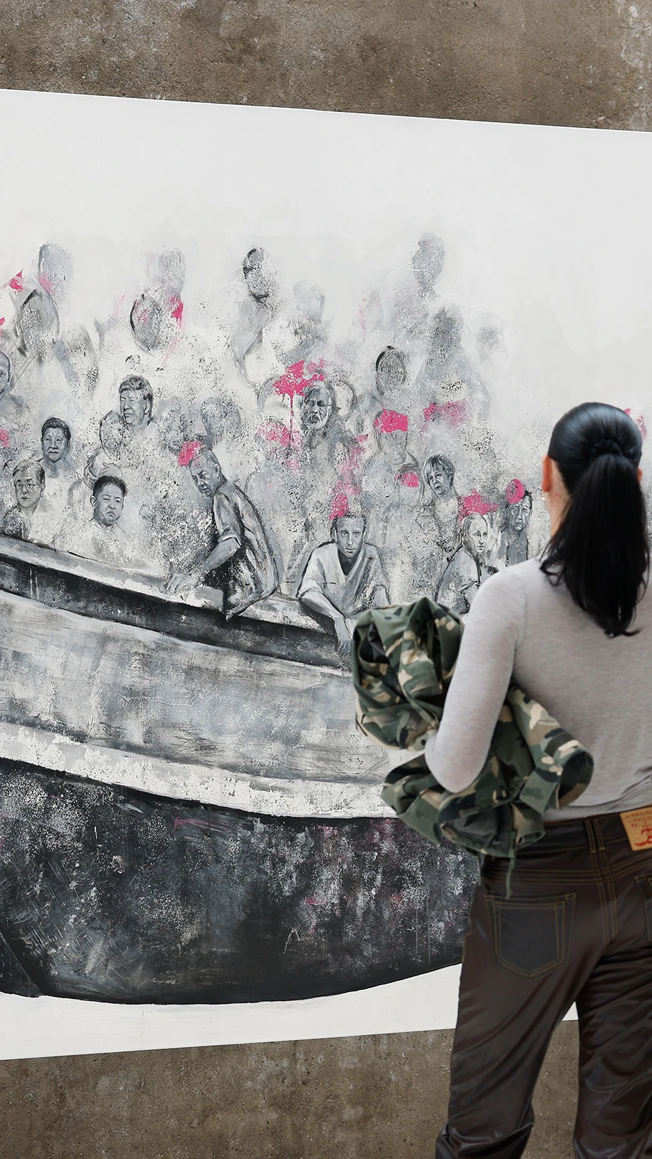 A man and woman observe a large mural of people crowded in a boat, wearing pink life vests. The scen