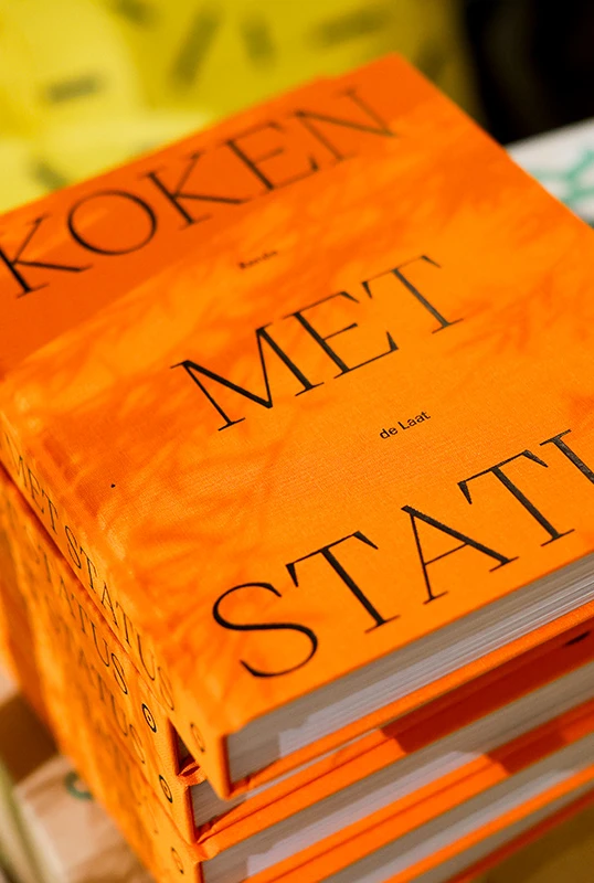 een oranje boek met de titel koken met status ligt op een stapel, sfeervol verlicht