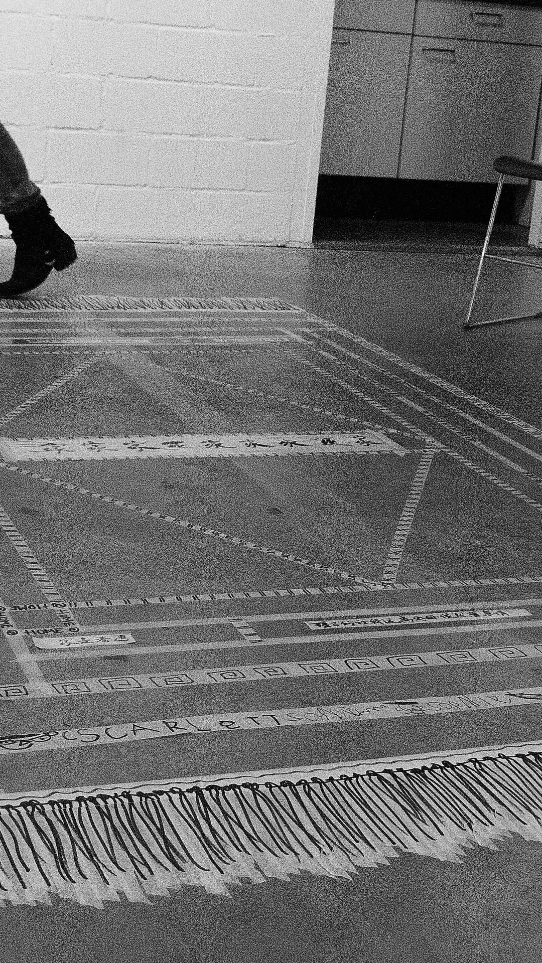 A person's legs and boots walk past a geometric design on the gallery floor.