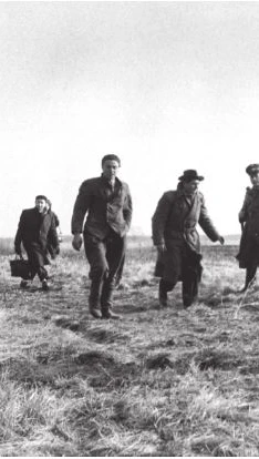 A group of people walking across a grassy field in a black-and-white photograph.