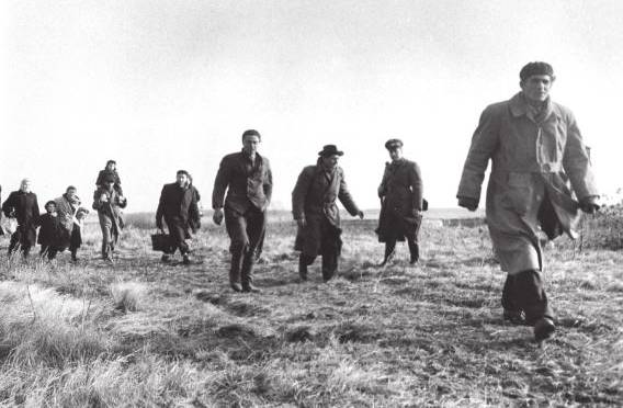 A group of people walking across a grassy field in a black-and-white photograph.