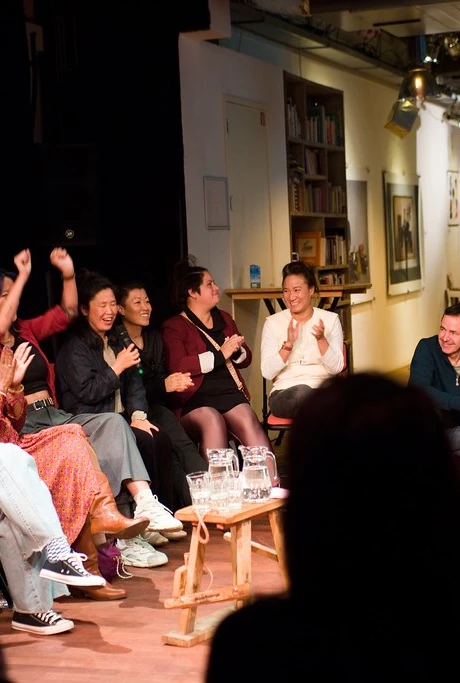 A group of people seated in a semi-circle indoors, clapping and cheering with joy.