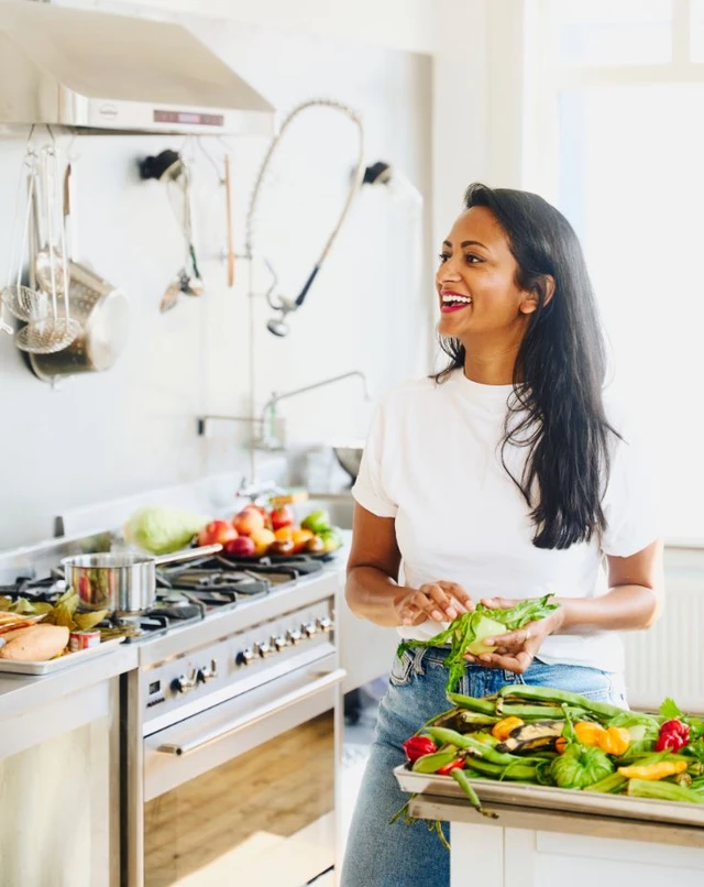 Een vrouw van Hindoestaanse afkomst in een keuken met een wit shirt en spijkerbroek aan.