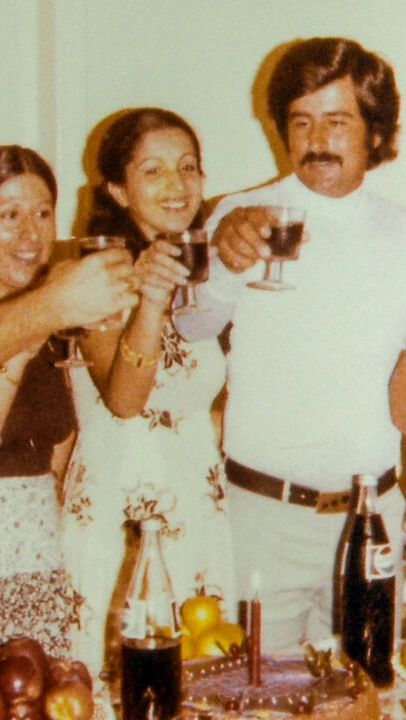 A group of seven people stand closely together indoors, smiling and raising glasses in a toast. A ta