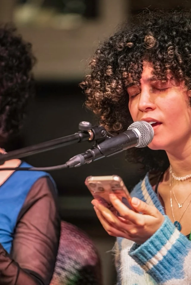 Two women with curly hair perform on stage.