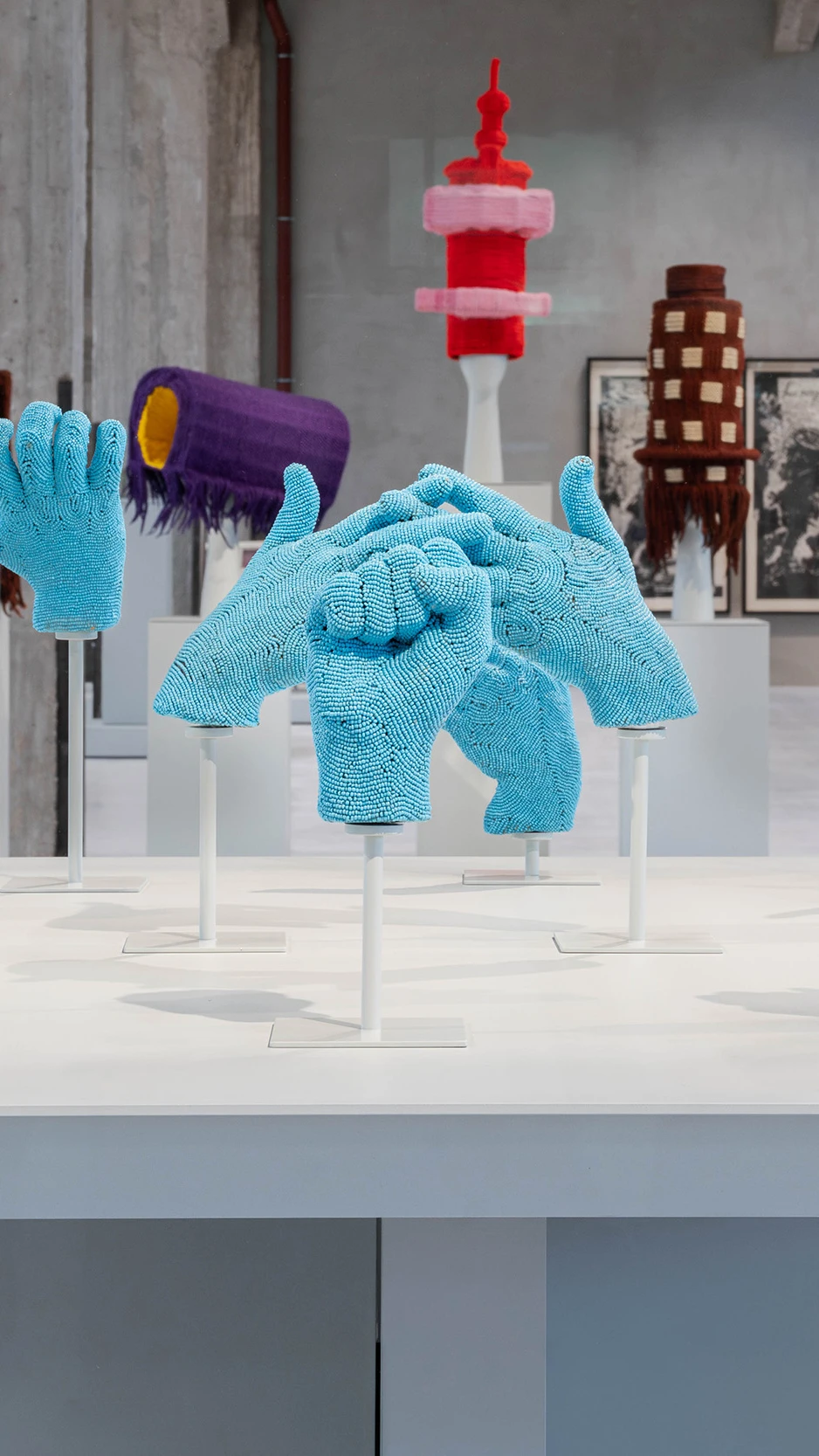 Een verzameling blauwe, met kralen versierde handen, in een vitrine in een moderne galerie.