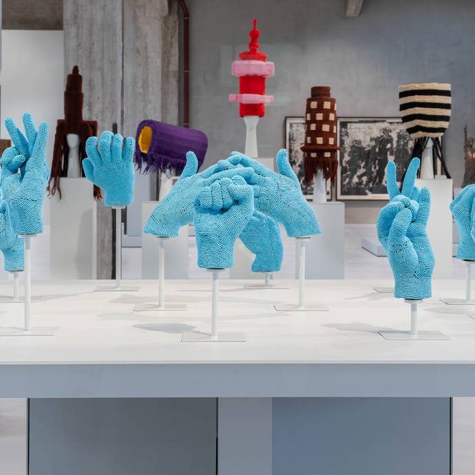 Een verzameling blauwe, met kralen versierde handen, in een vitrine in een moderne galerie.