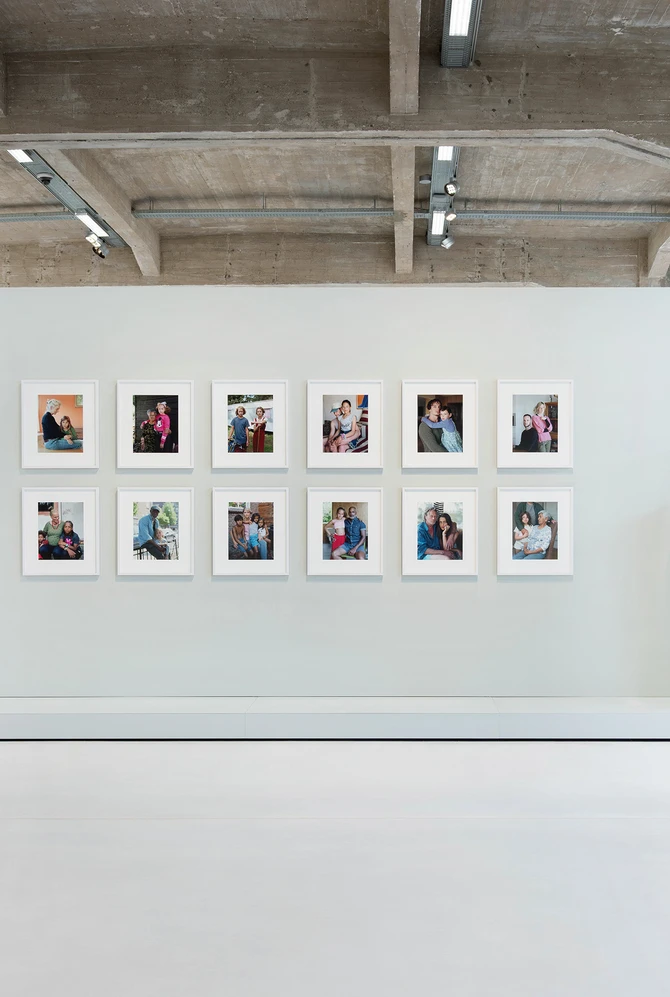 Een moderne tentoonstellingszaal waar je recht op een muurtje kijkt met in een grid foto's