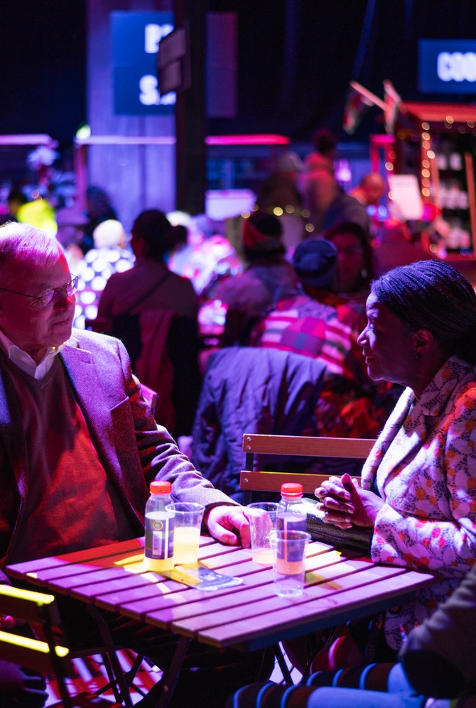 Een witte man en zwarte vrouw zitten tijdens Brasadag samen aan tafel met wat lekkers te drinken