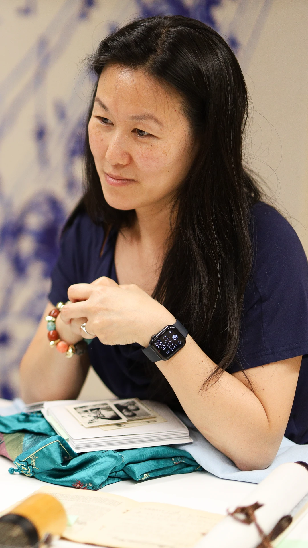 Three women sit at a table engaged in conversation, with photos and items spread out.