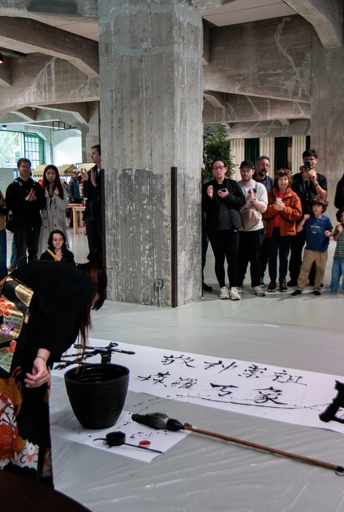 A Japanese calligraphy artist performs live as visitors gather around at CAMERA JAPAN.