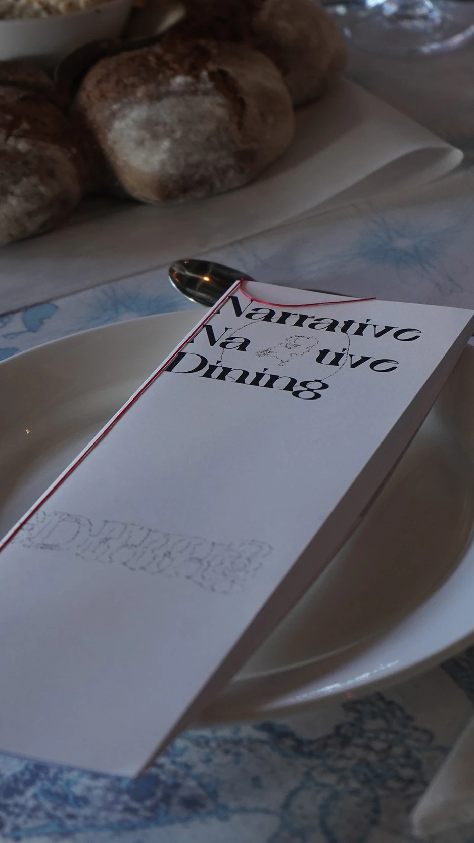 Elegant table setting with a patterned blue dutch tablecloth, menu labeled "Narrative Dining,"