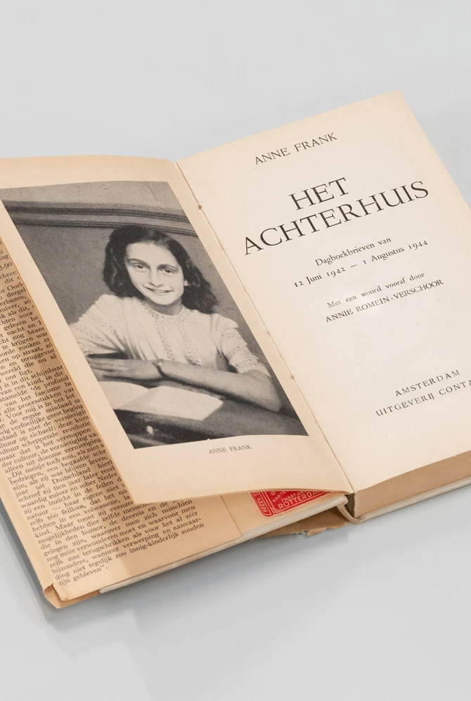 An open book titled "Het Achterhuis" by Anne Frank, featuring a photograph of a young Anne Frank.