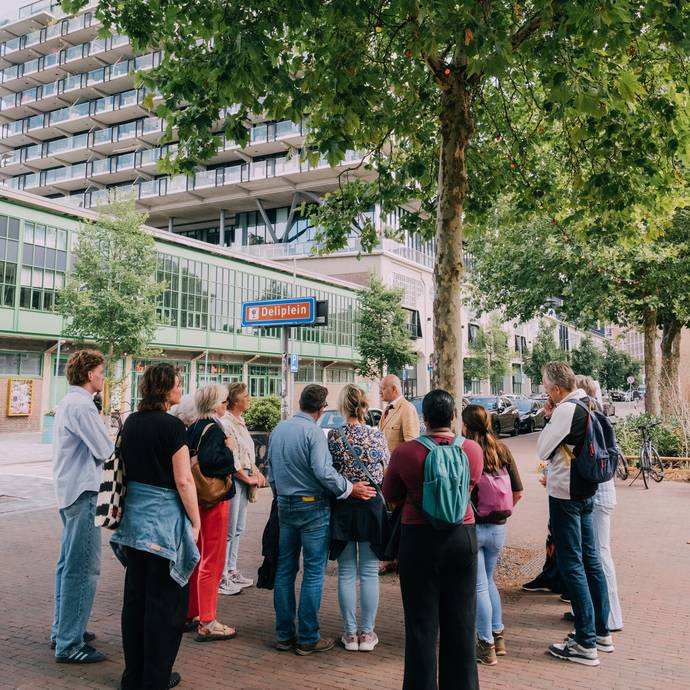 een groepje mensen staat om een verteller heen. op een straatbord staat 'deliplein'