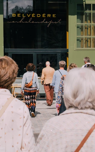 de verteller gaat de groep mensen voor om een gebouw in te gaan.Op de gevel: verhalendepot belvedere