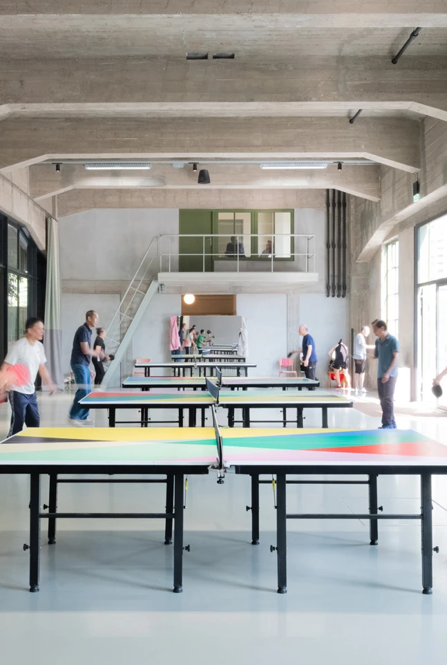 Een groep mensen speelt een toernooi tafeltennis in een loodsachtige ruimte