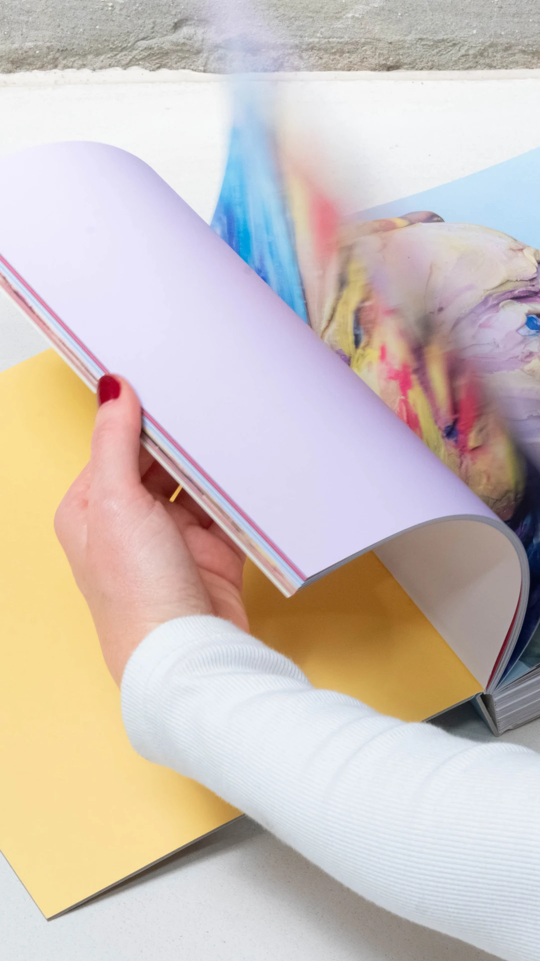 twee handen bladeren door een boek op een neutrale achtergrond. je ziet fotos van gekleide figuren