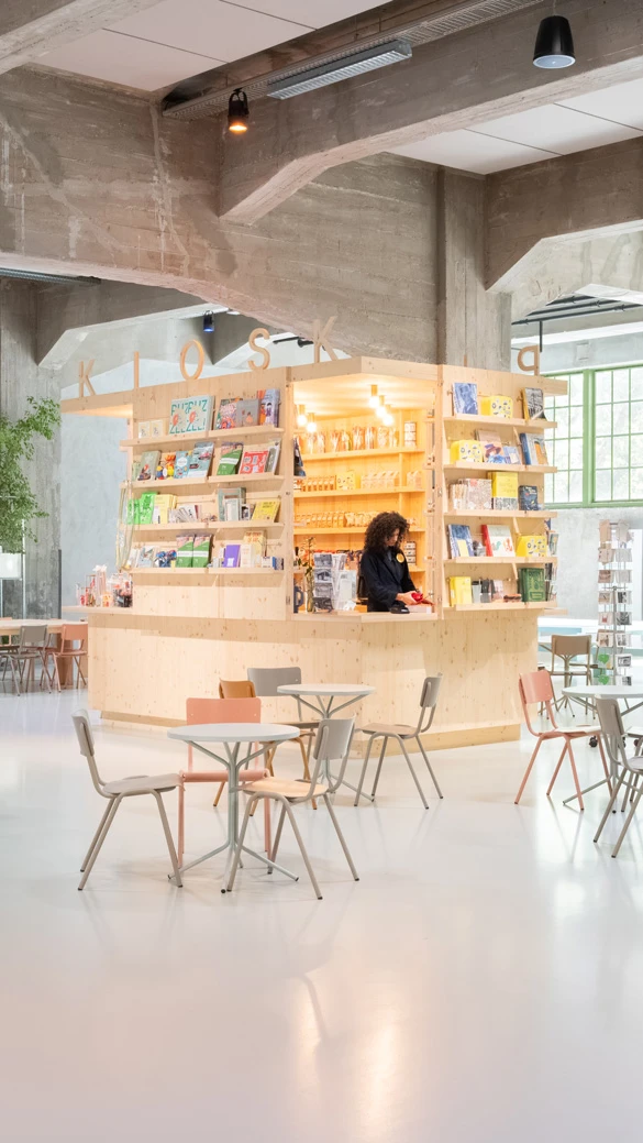 Een modere, ruime ruimte, met een licht houten kiosk en kleine tafels in een cafe opstelling