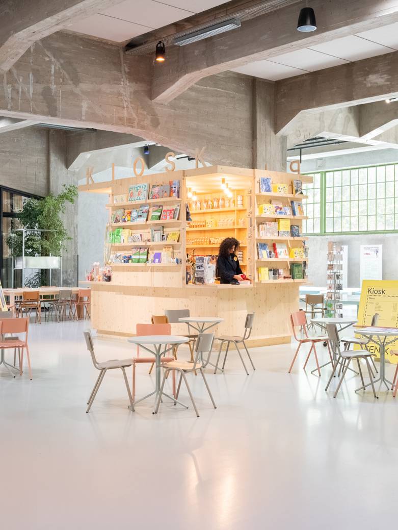 Een modere, ruime ruimte, met een licht houten kiosk en kleine tafels in een cafe opstelling