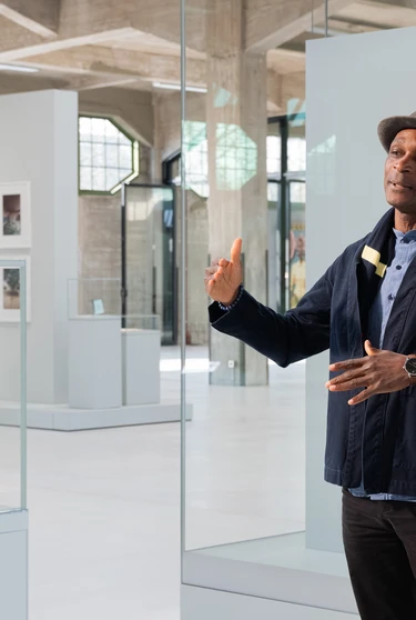 A person stands in Fenix, gesturing while speaking. They wear a hat and dark jacket.