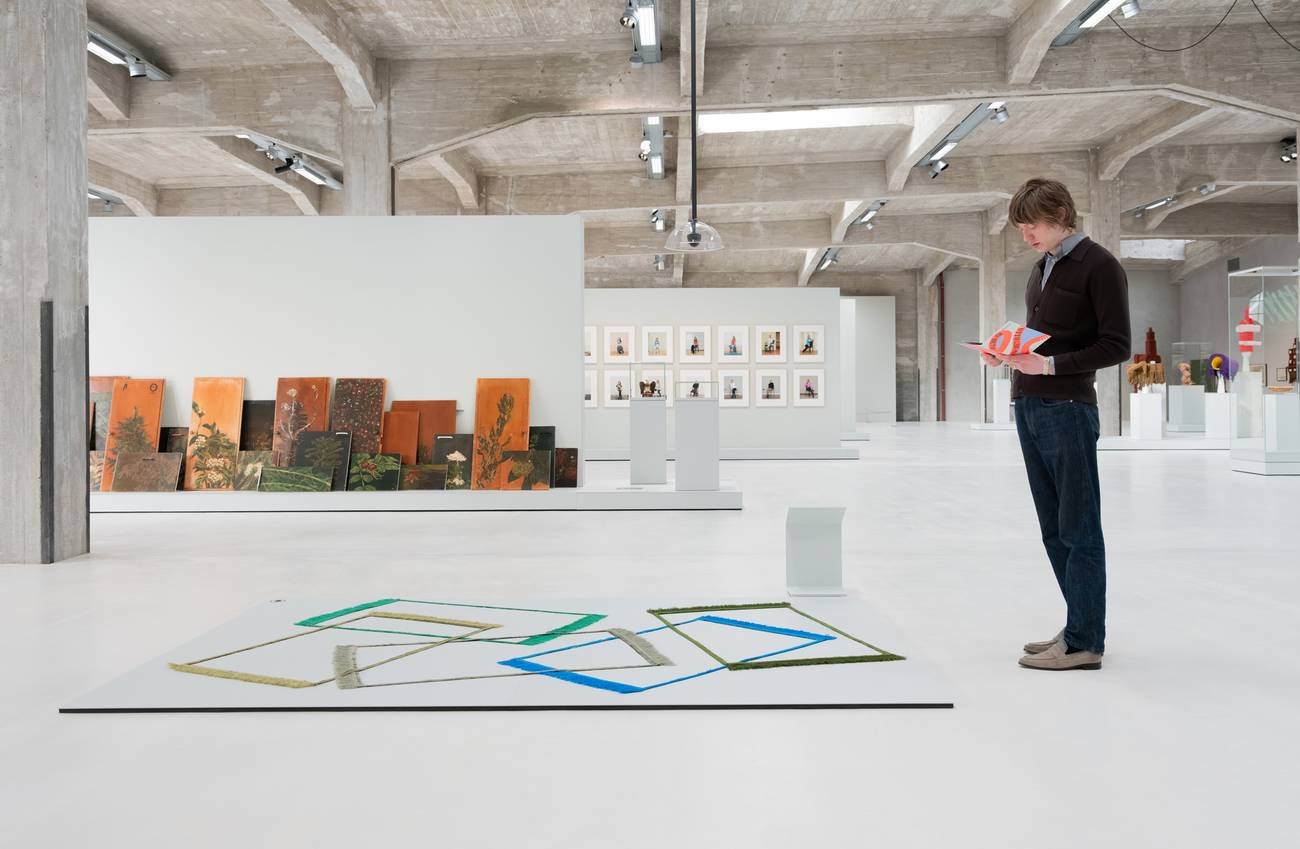 A person reads a folder in a spacious art gallery with a geometric artwork on the floor