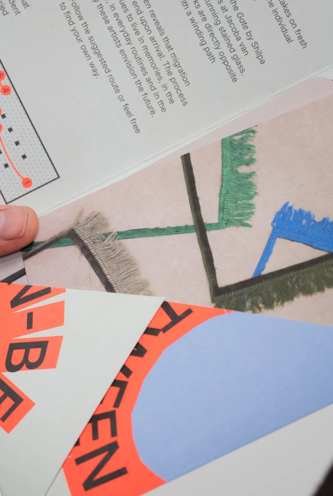 Two hands hold colorful abstract art pamphlets with bold graphics and text.