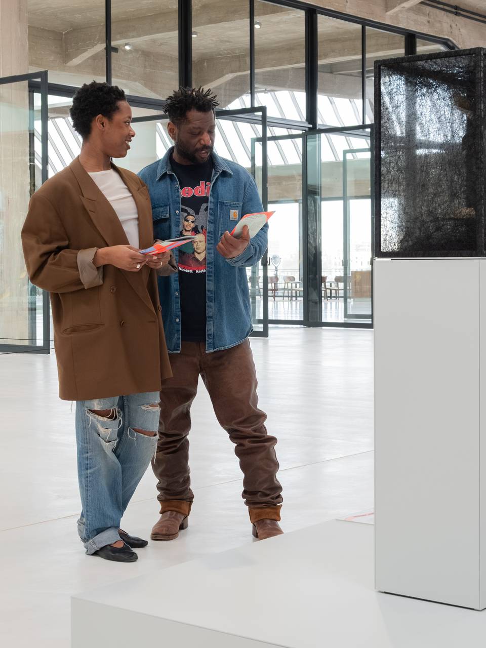 Two people admire a mesh sculpture on a pedestal in a modern art gallery.