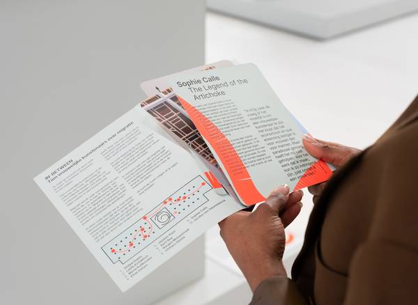 twee handen houden een mapje met kaarten vast, met een plattegrond en uitleg over een kunstwerk