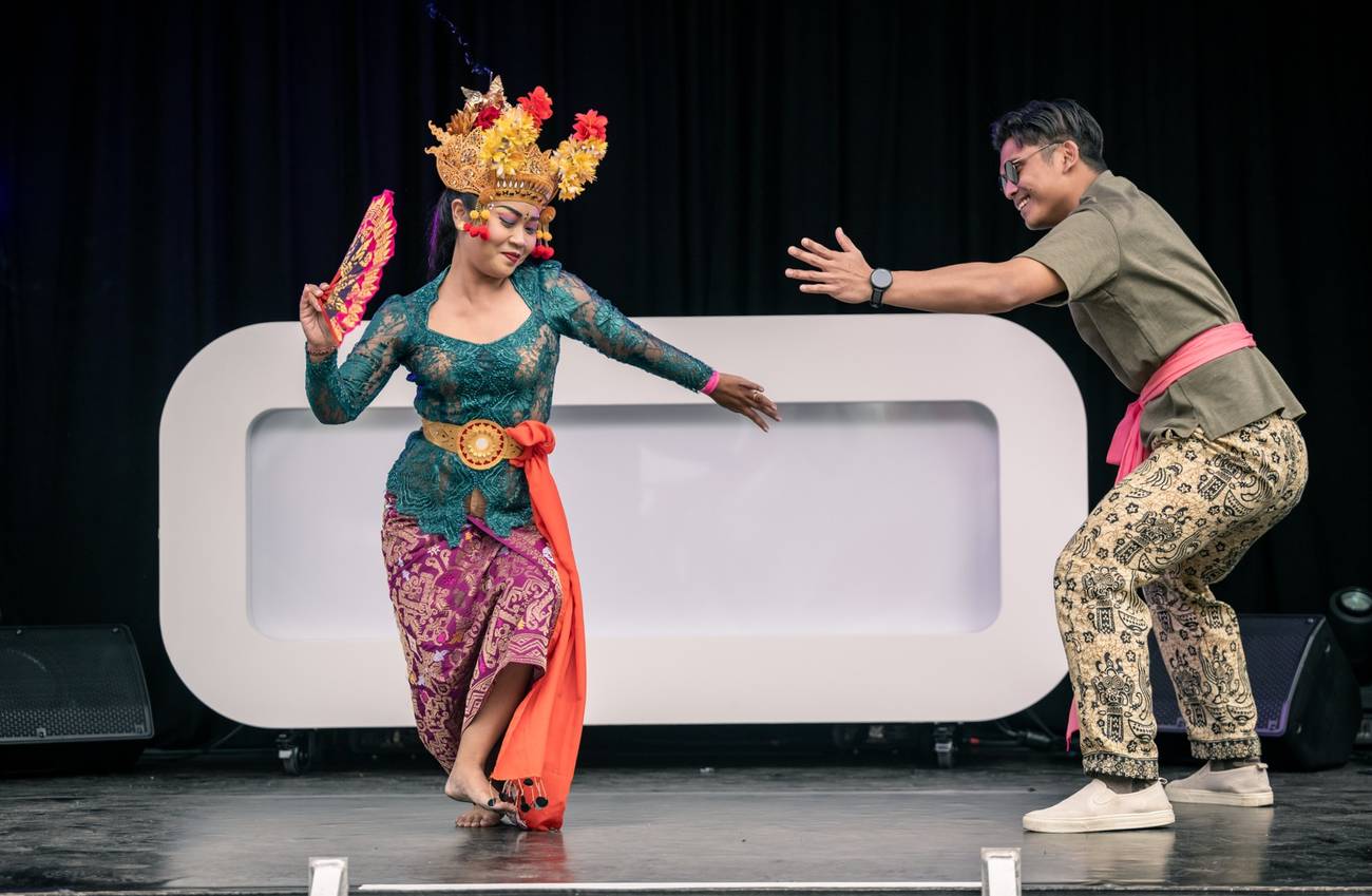 Two dancers in traditional Balinese clothing perform together on a stage.