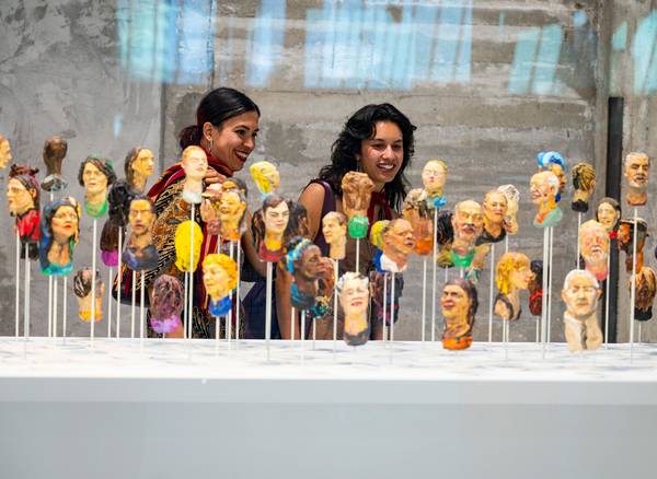 Two women in Fenix admire colorful clay busts on thin sticks. The display is vibrant and diverse