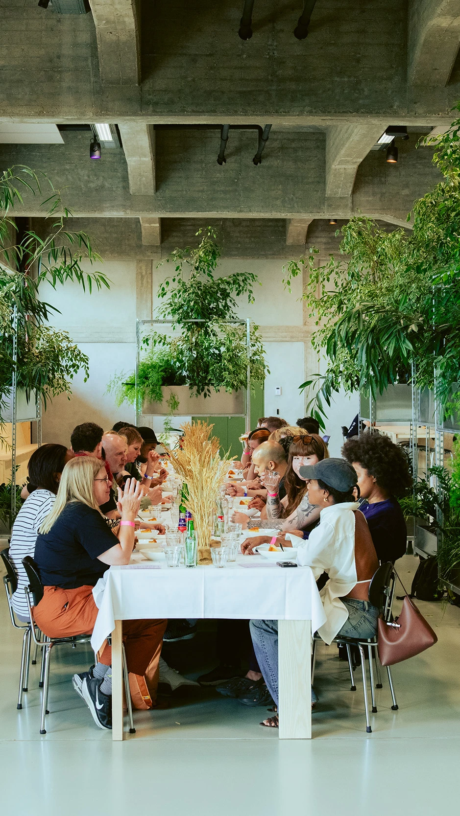 en lange eettafel met mensen die samen lunchen in een lichte ruimte met betonnen plafonds en veel gr