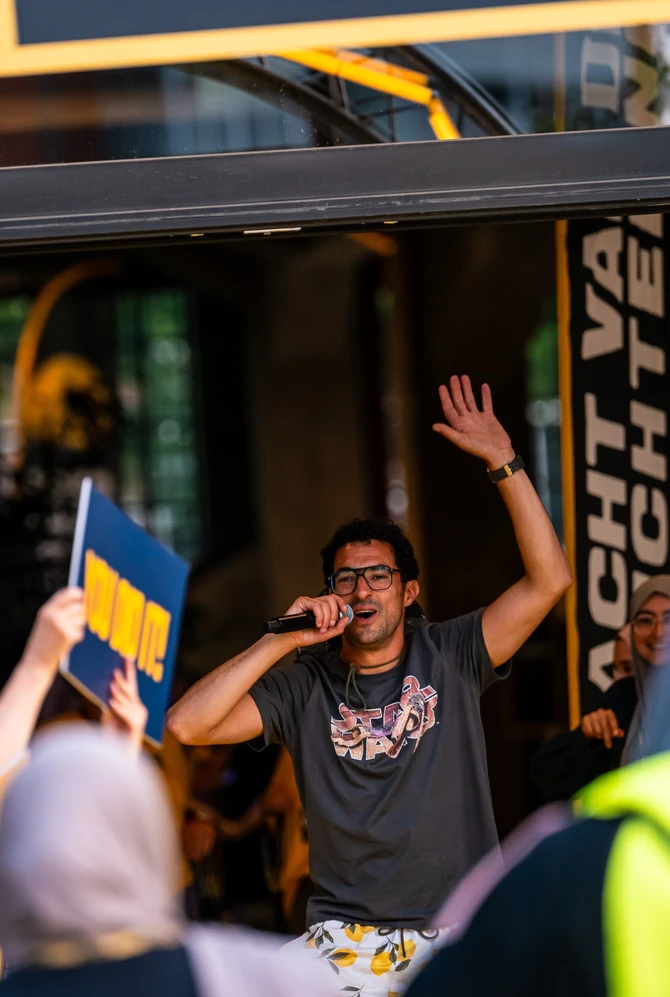 A lively scene featuring a man with a microphone, hand raised, surrounded by cheering people in yell