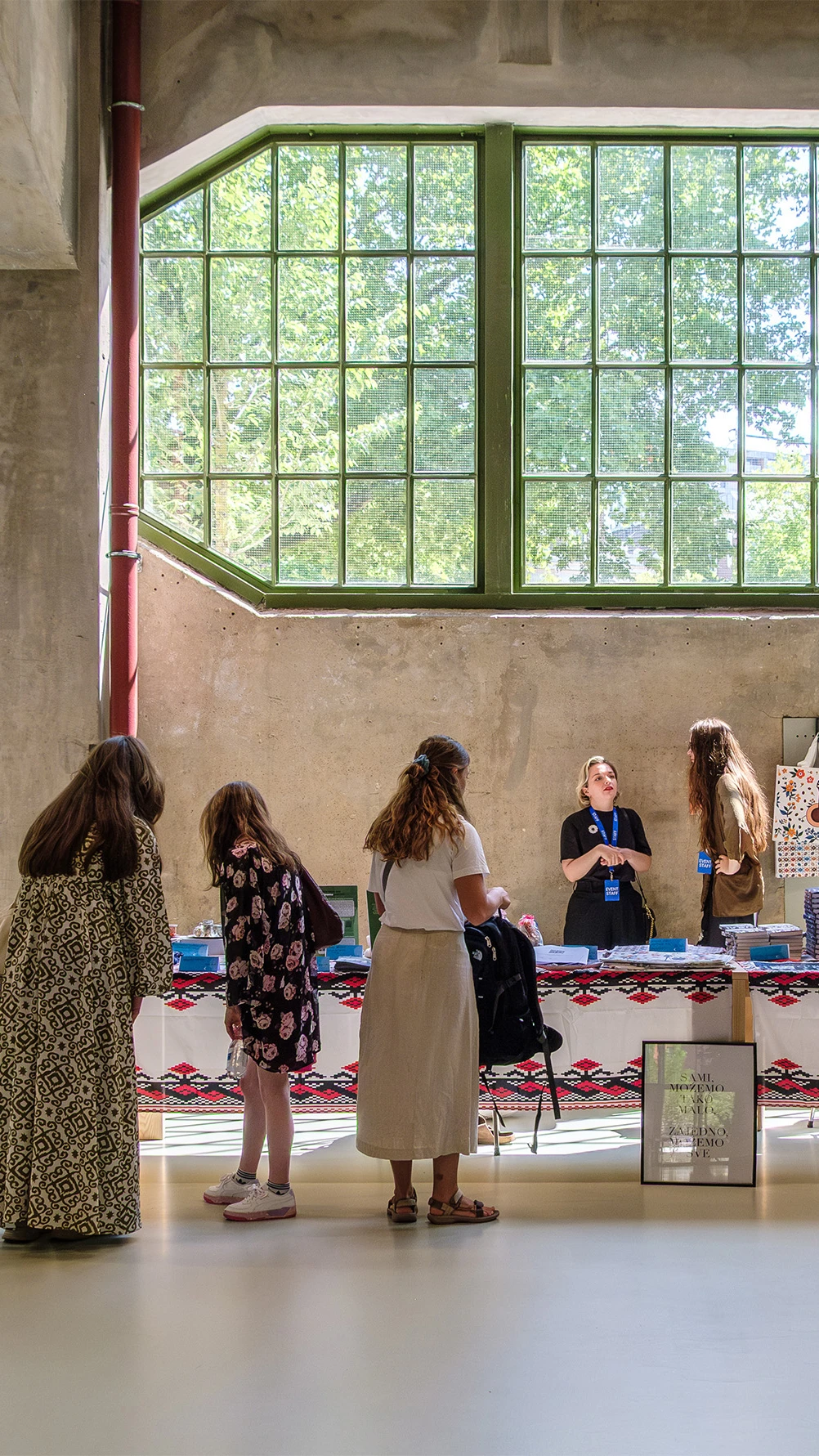 een lange tafel waar mensen omheen staan, op tafel liggen boeken en folders