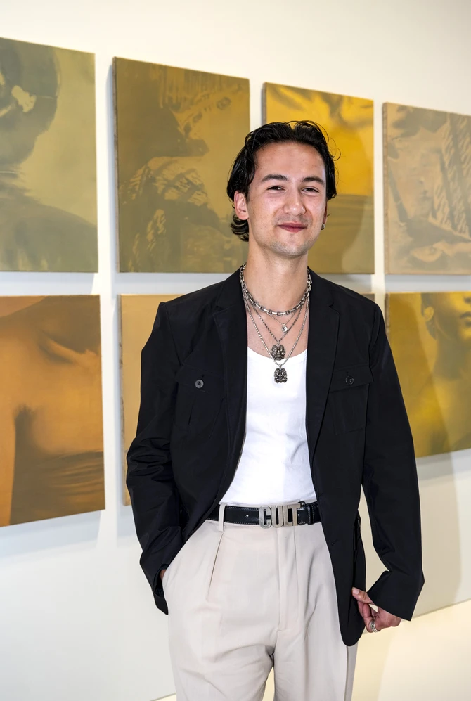 Portrait of an artist standing before golden-toned artworks.