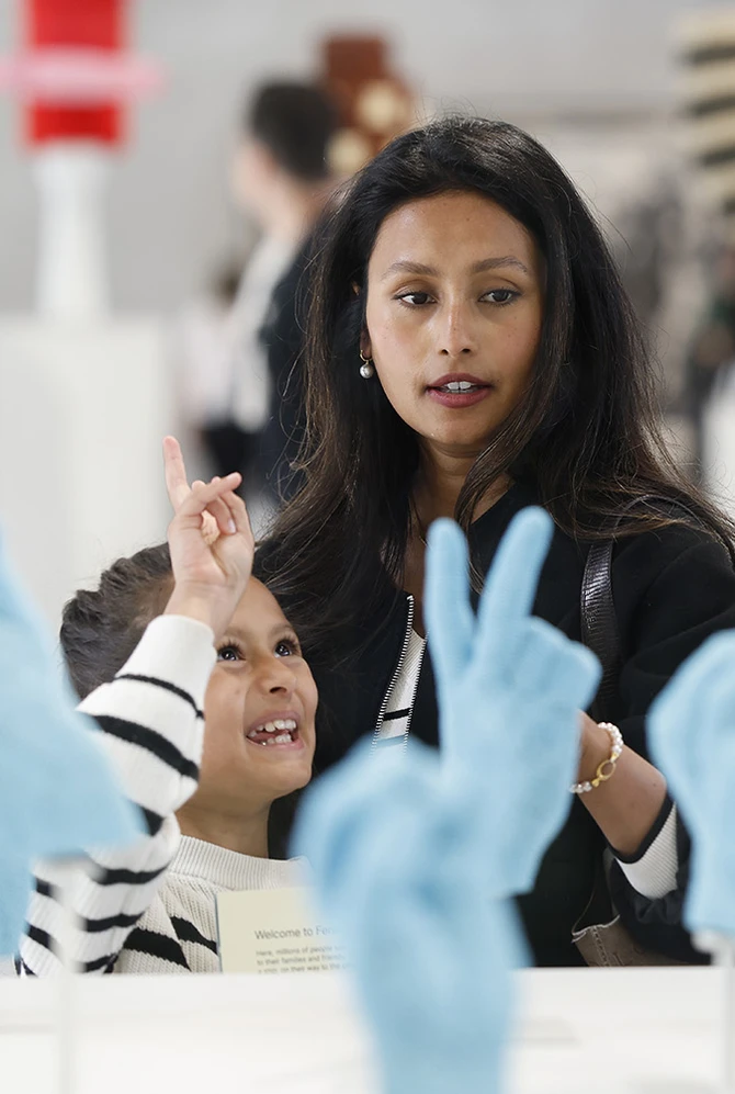 A woman and child observe bright blue sculpted hands in a gallery.