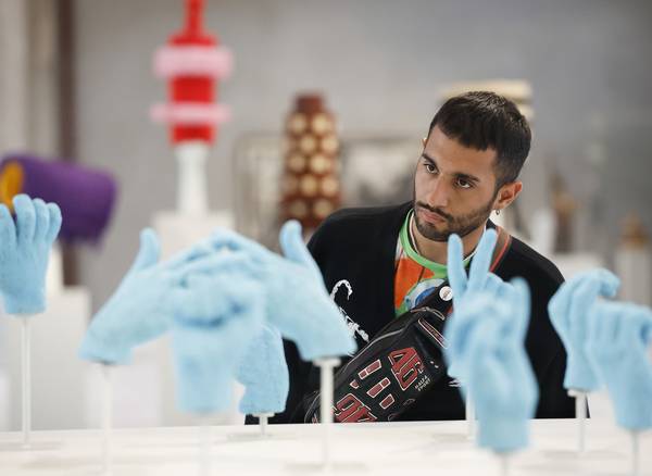 A man attentively examines an art display of multiple blue, beaded hand sculptures on stands.