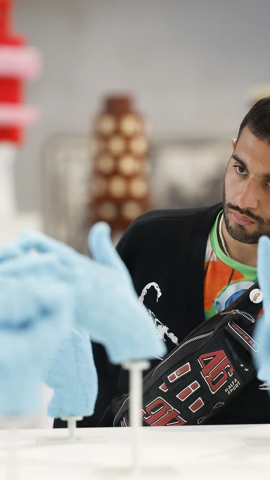 A man attentively examines an art display of multiple blue, beaded hand sculptures on stands.