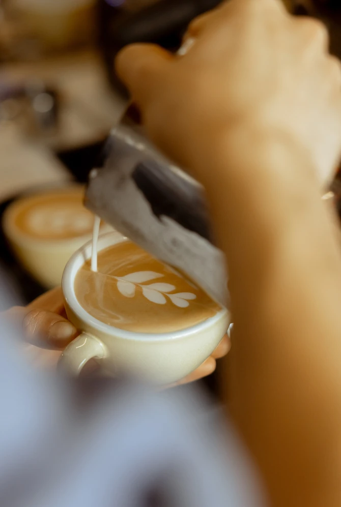 Barista creating intricate latte art with frothed milk, forming a delicate leaf pattern on coffee