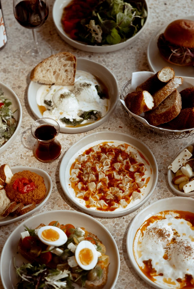 A table with assorted dishes, including salads, dips, bread, eggs, and yogurt, surrounded by glasses