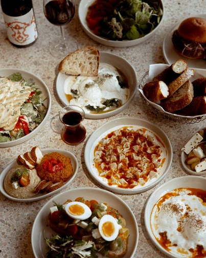 A table with assorted dishes, including salads, dips, bread, eggs, and yogurt, surrounded by glasses