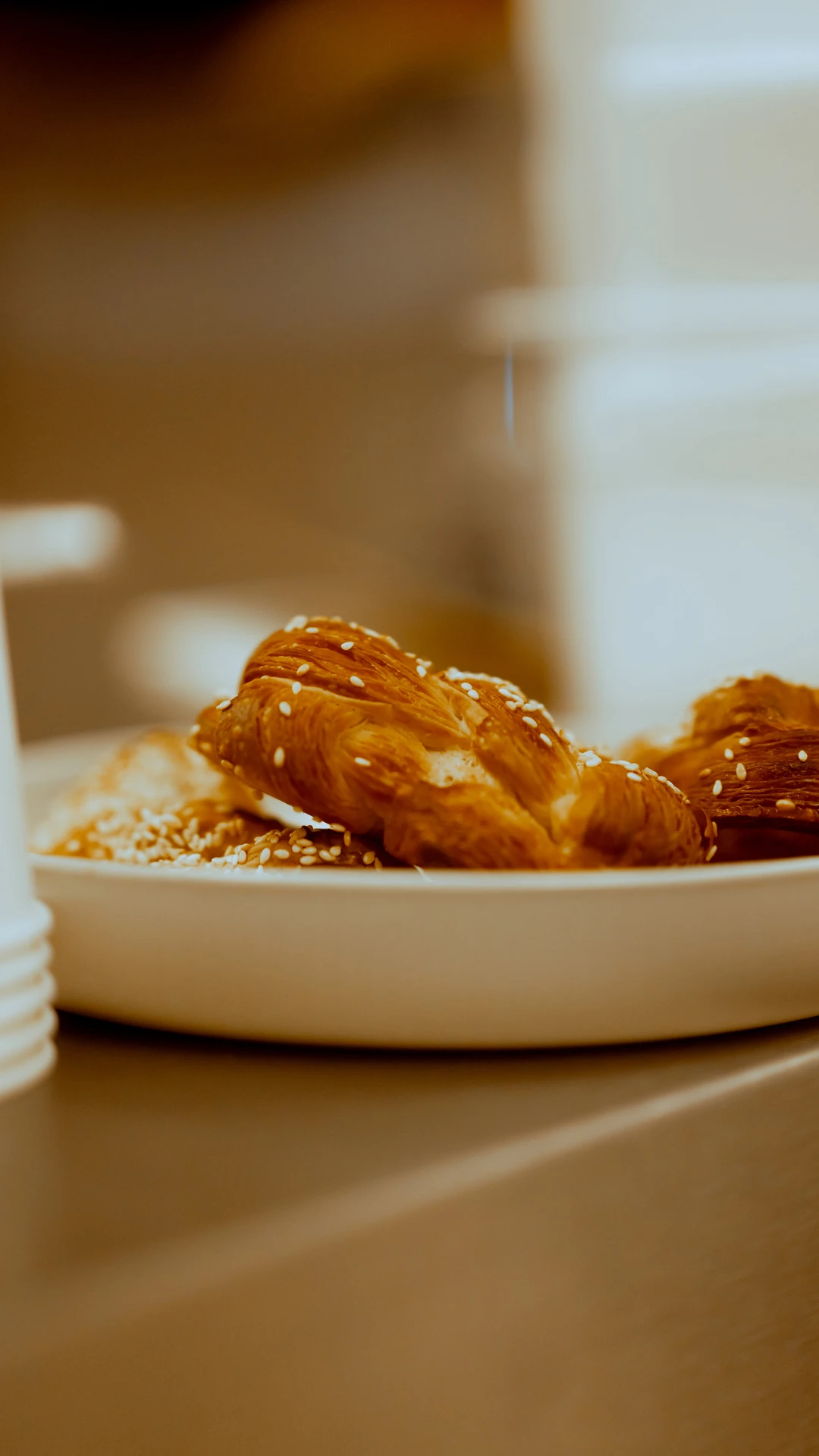 Close-up of a plate with flaky sesame-seeded pastries on a wooden surface.