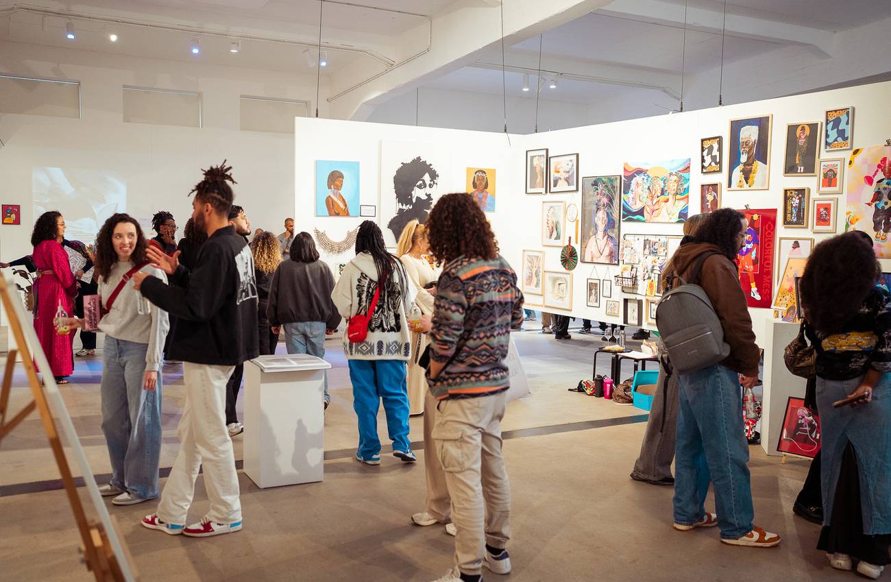 Art gallery with diverse people viewing colourful portraits and abstract art on white walls.