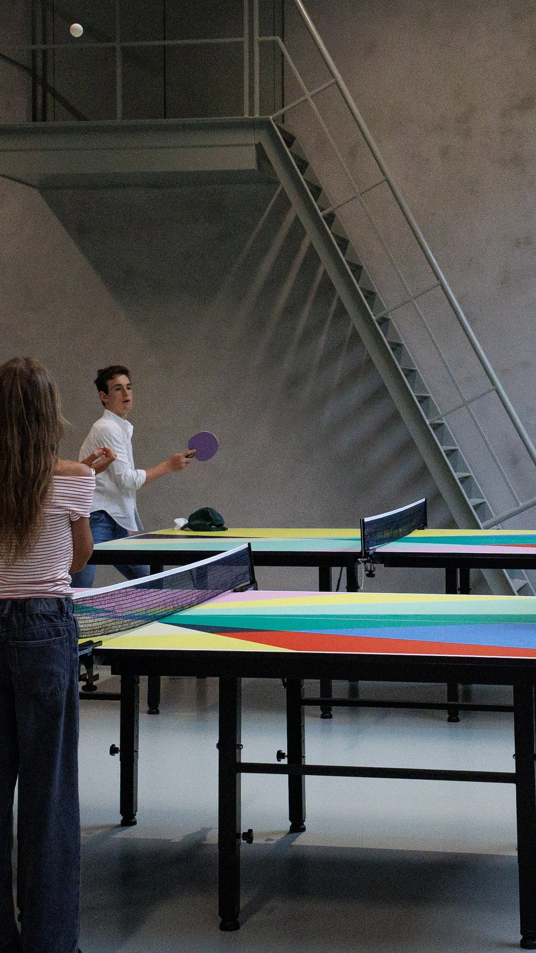 Kinderen en volwassenen spelen samen tafeltennis aan kleurrijke tafels in een grote, lichte binnenru