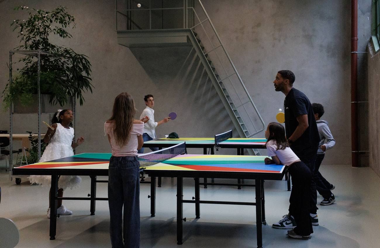 Kinderen en volwassenen spelen samen tafeltennis aan kleurrijke tafels in een grote, lichte binnenru